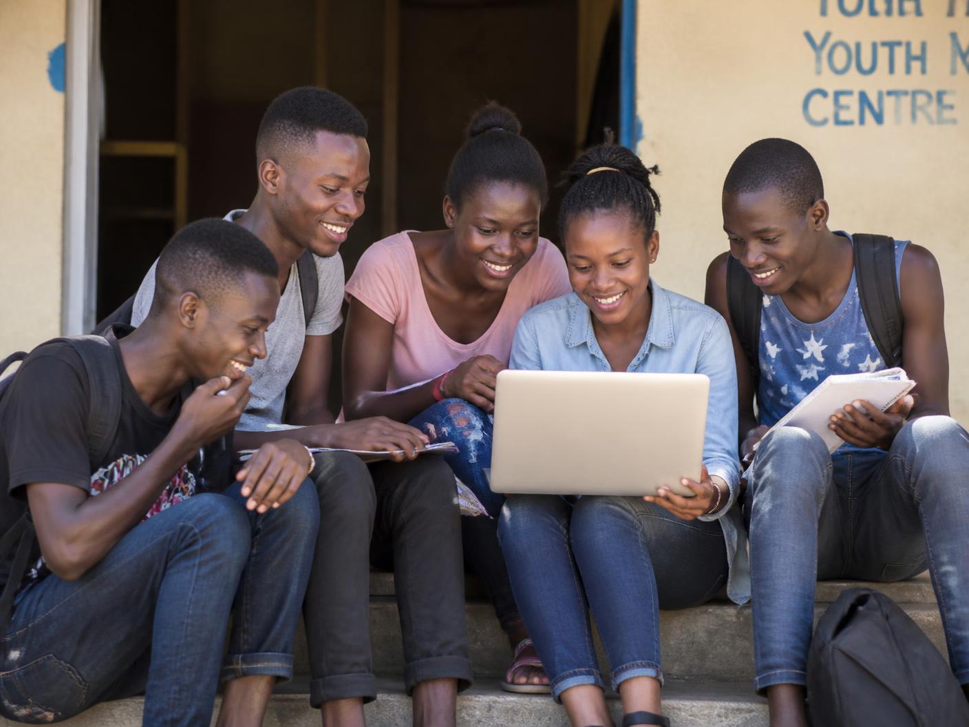 Five teenagers sitting on steps together, sharing a laptop and notebooks